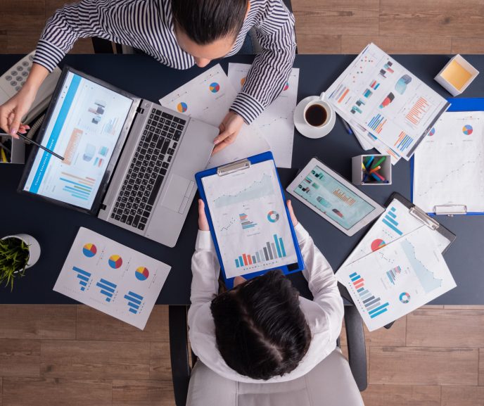 Top viewTop view of manager and employee doing teamwork in business office , looking at charts on laptop display. Finance paperwork with charts at workplace. Discusing financial plan.